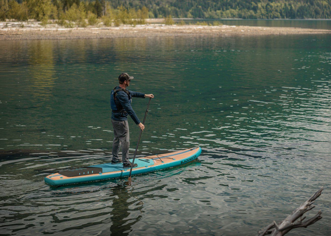 A person stand-up paddleboarding on a calm forested lake